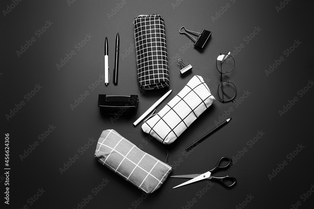 Different pencil cases, eyeglasses and stationery on dark background