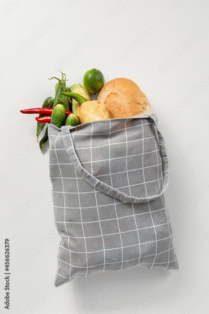 Eco bag with different vegetables and bread on white background