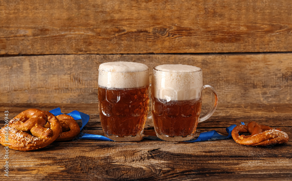 Mugs of fresh beer and pretzels on wooden background. Oktoberfest celebration