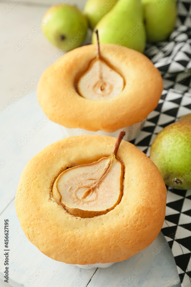 Wooden board with tasty pear pot pies and fresh fruits on light background