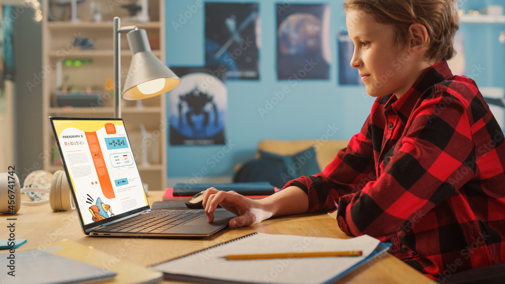 Smart Young Boy Researching Homework Topic from an Exercise Book on Laptop Computer. Happy Teenager 