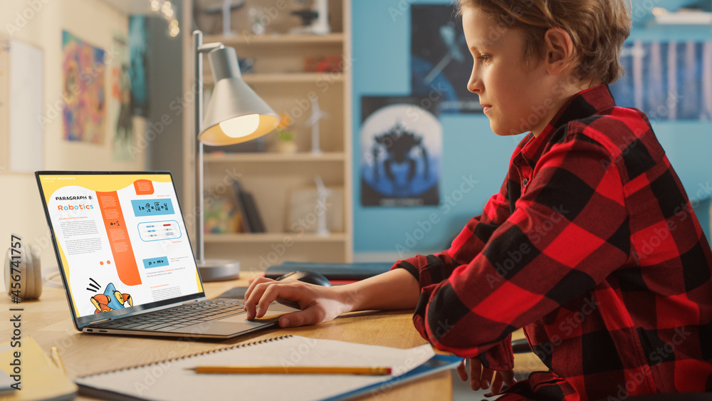 Smart Young Boy Researching Homework Topic from an Exercise Book on Laptop Computer. Happy Teenager 