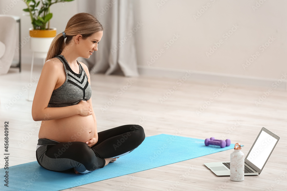 Young pregnant woman practicing yoga at home