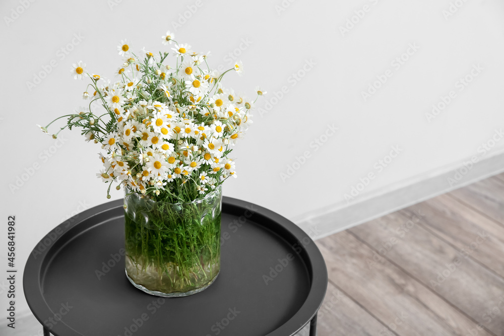 Vase with chamomiles on table near light wall