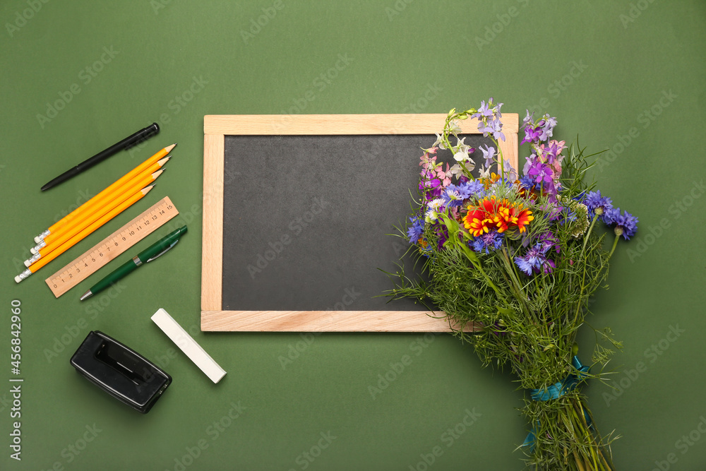 Blank chalkboard, bouquet of flowers and stationery on color background