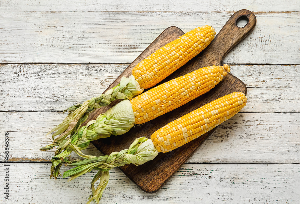 Board with fresh corn cobs on light wooden background