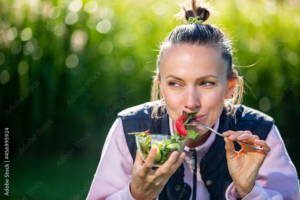 美丽的高加索女人在绿色自然背景下吃沙拉