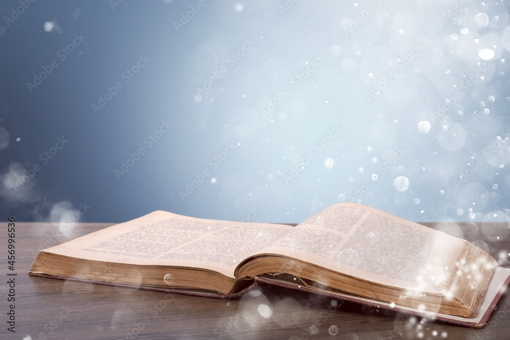 Open old book on wooden table and dark background with shine and flying particles