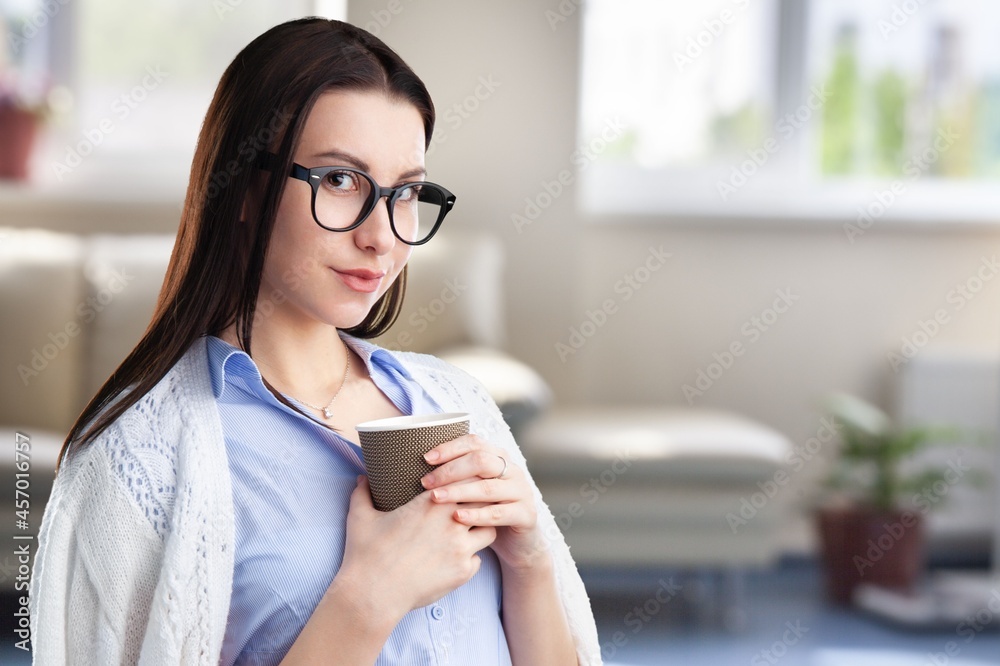 Portrait of a joyful young woman enjoying a cup of coffee or tea at home.