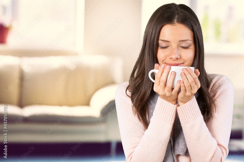 Portrait of a joyful young woman enjoying a cup of coffee or tea at home.