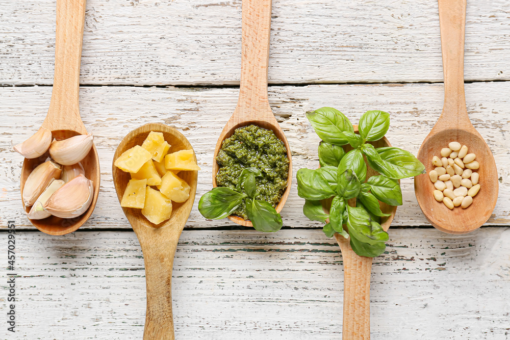 Spoons with tasty pesto sauce, cheese, pine nuts and garlic on light wooden background