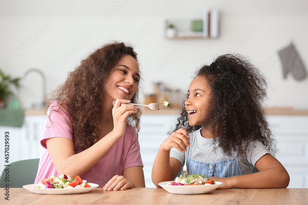 African-American little girl with her mother eating fresh salad in kitchen