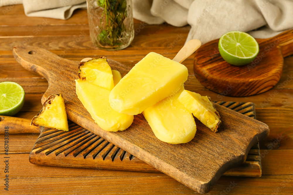 Board with tasty pineapple popsicles on wooden background