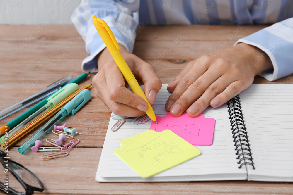 Woman writing word DONE on sticky note at table, closeup