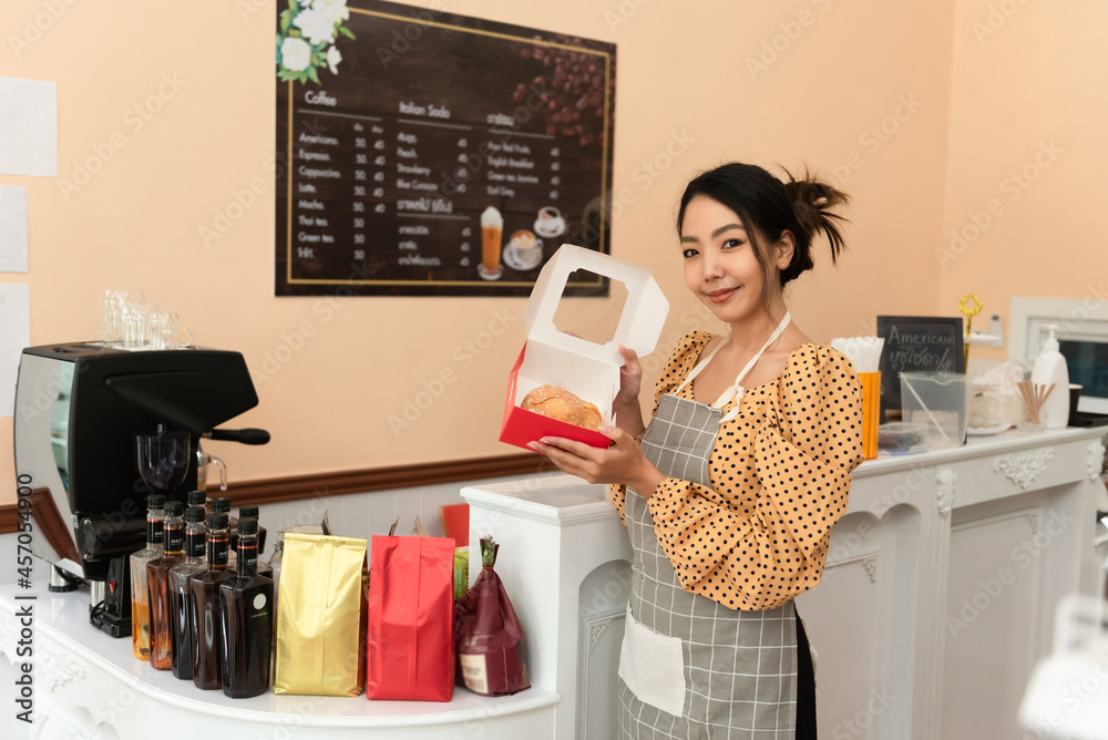 快乐的亚洲女面包师，拿着一篮子面包，在她的面包店工作。中年女性en