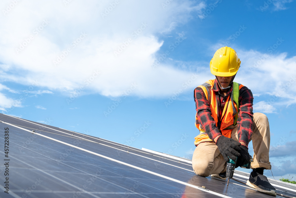 Solar panel technician with drill installing solar panels on roof at solar panel field,Environmental