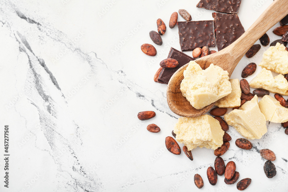 Spoon with cocoa butter, beans and chocolate on light background