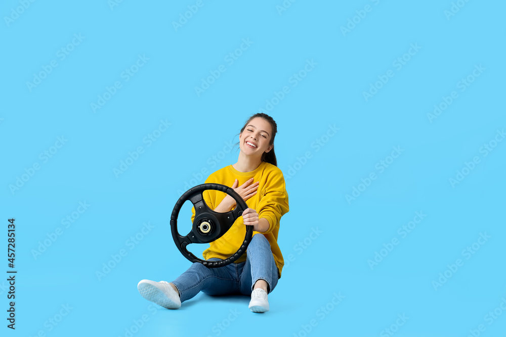 Young woman with steering wheel on color background