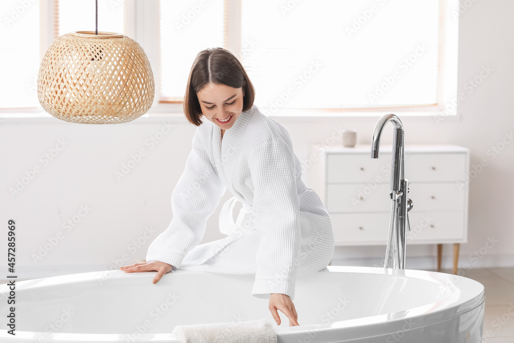 Young woman running bathtub with warm water at home