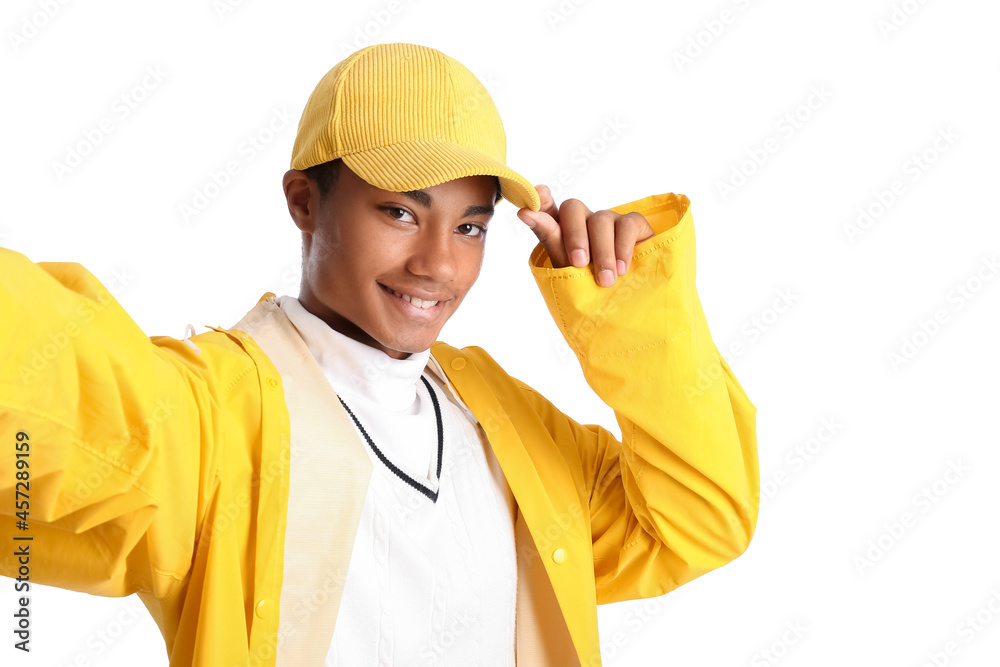 Handsome stylish African-American guy in raincoat taking selfie on white background