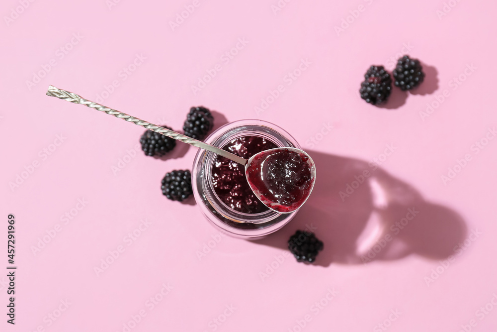 Jar and spoon with tasty blackberry jam on color background