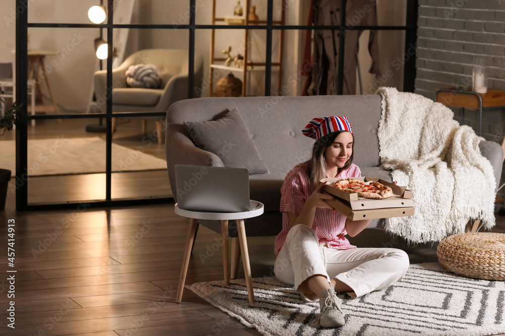 Beautiful young woman eating tasty pizza at home in evening