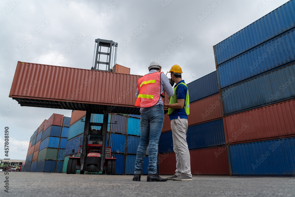 Industrial worker works with co-worker at overseas shipping container yard . Logistics supply chain 