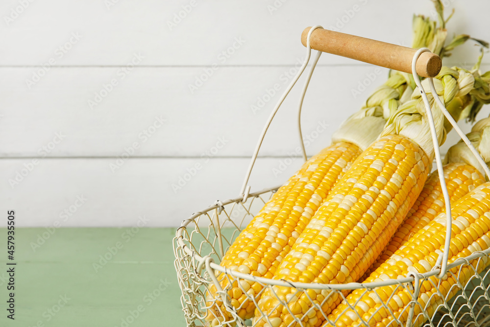 Basket with fresh corn cobs on light wooden background