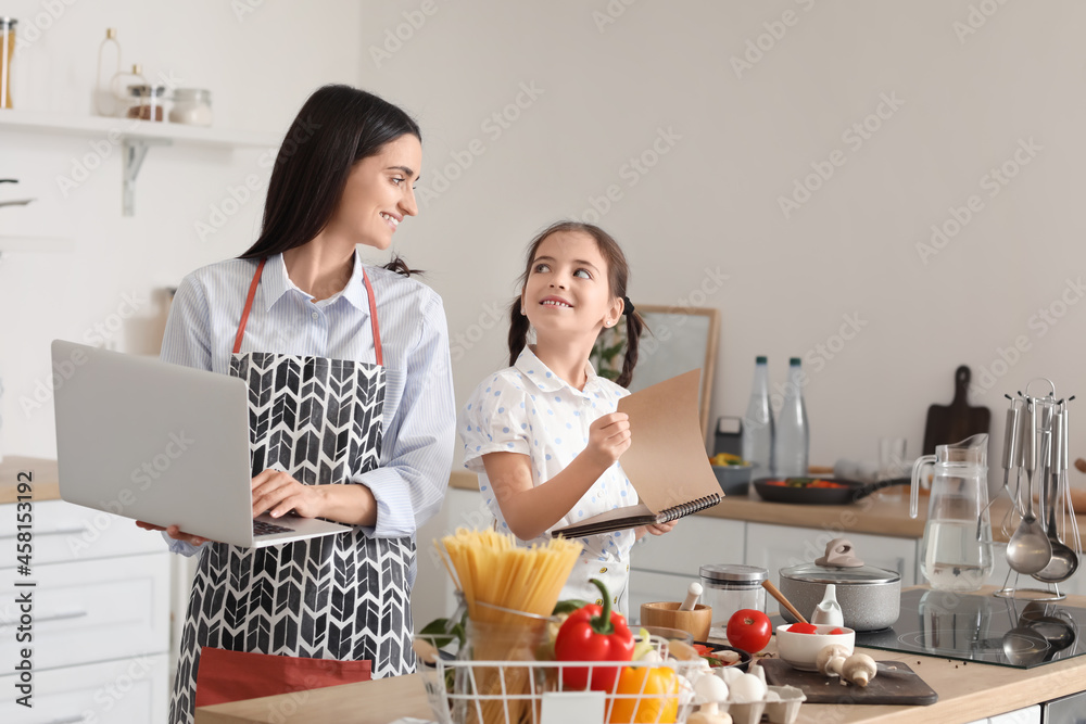 年轻的母女带着笔记本电脑在家里的厨房里一起做饭