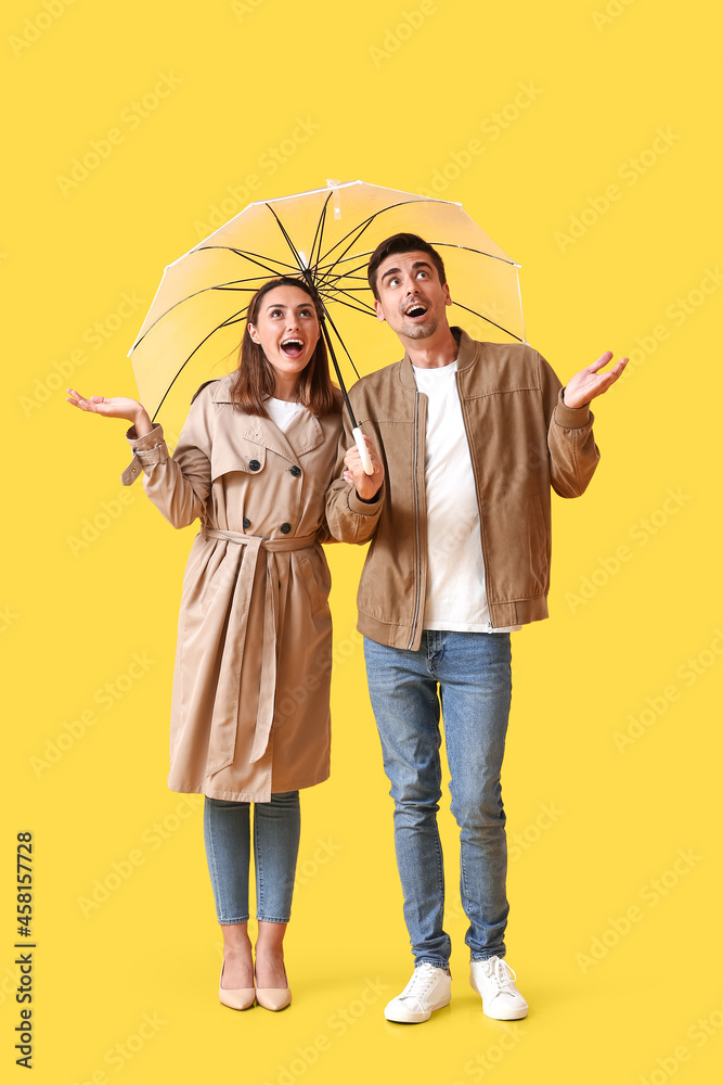 Young couple with umbrella on color background