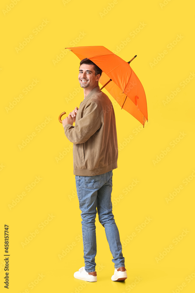 Handsome young man with umbrella on color background