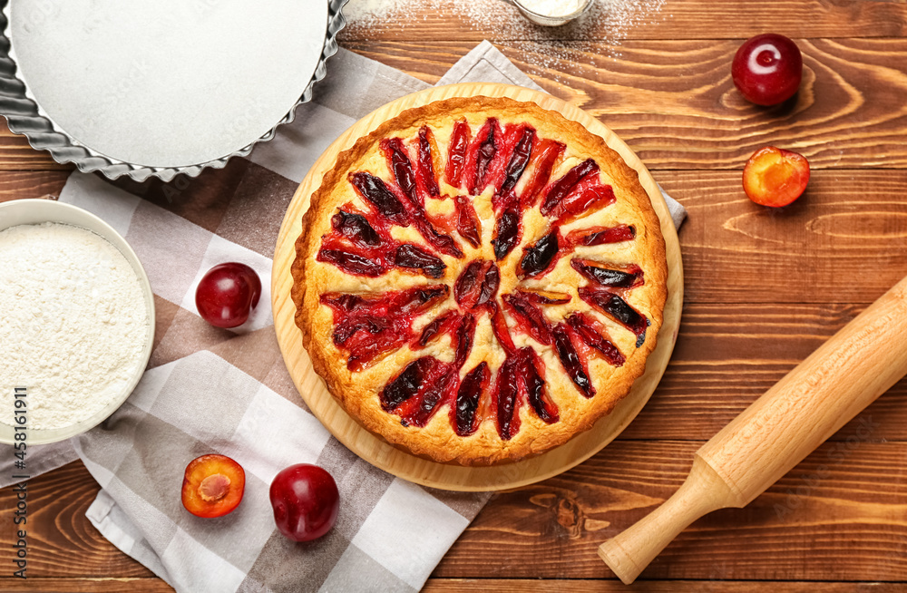 Board with tasty plum pie on wooden background