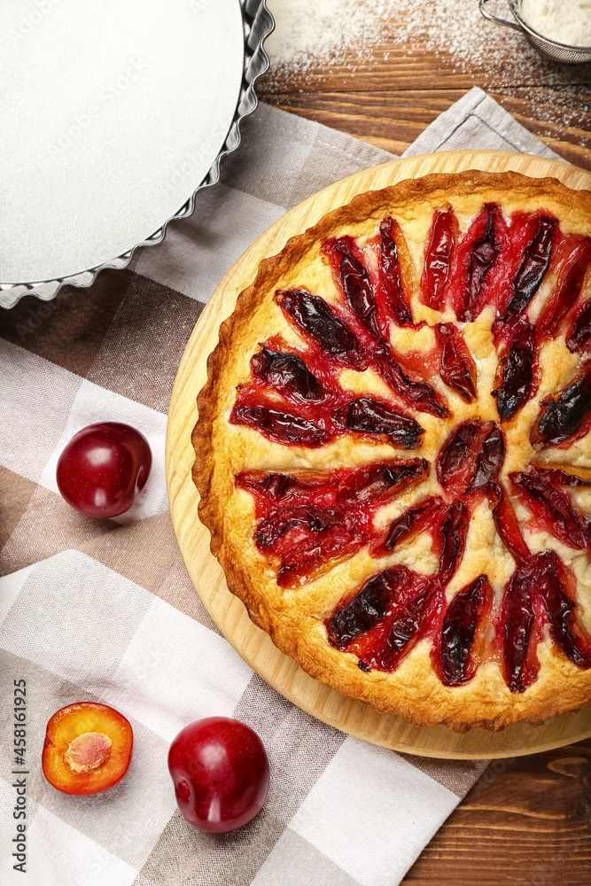 Board with tasty plum pie on wooden background