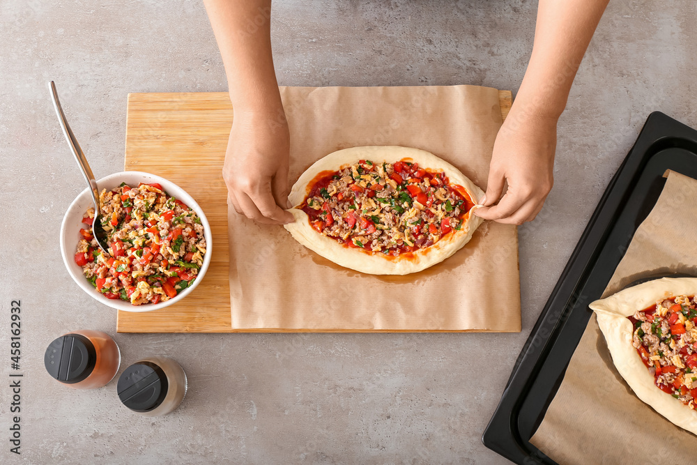 Woman preparing Turkish Pizza on grey background