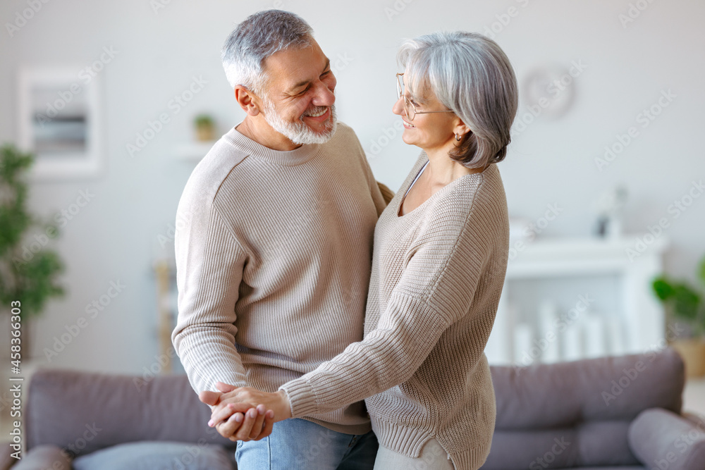 Happy senior couple in love looking at each other with tenderness, dancing together in living room