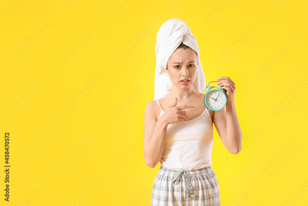 Upset young woman pointing at alarm clock on color background