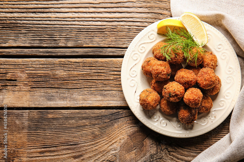 Plate with tasty cod cutlets with lemon on wooden background