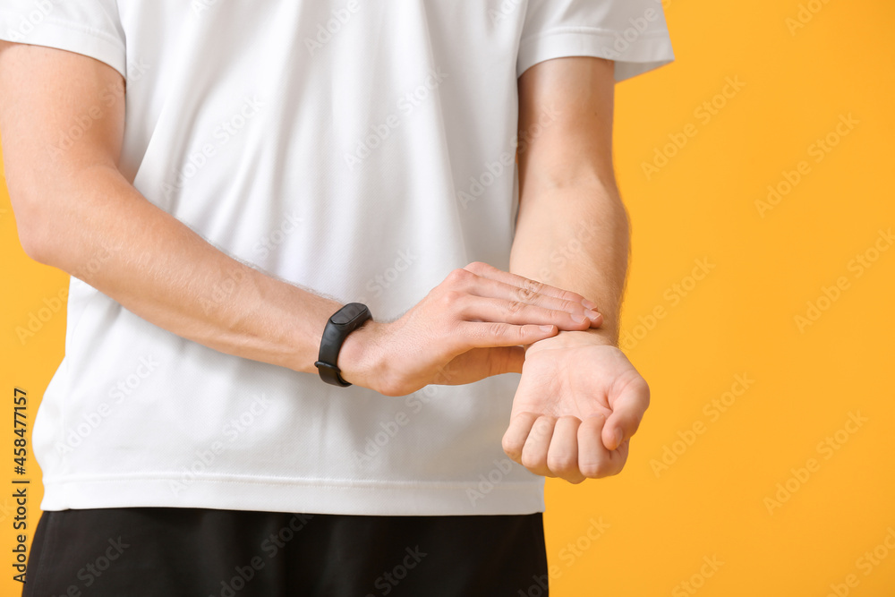 Sporty male runner checking pulse on color background