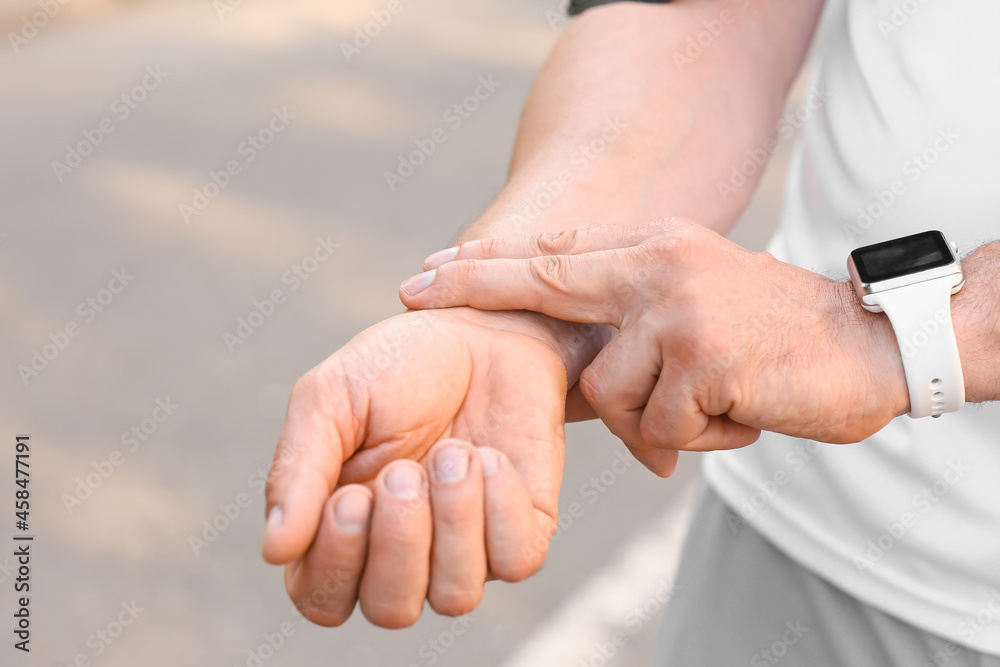 Male runner checking pulse outdoors, closeup