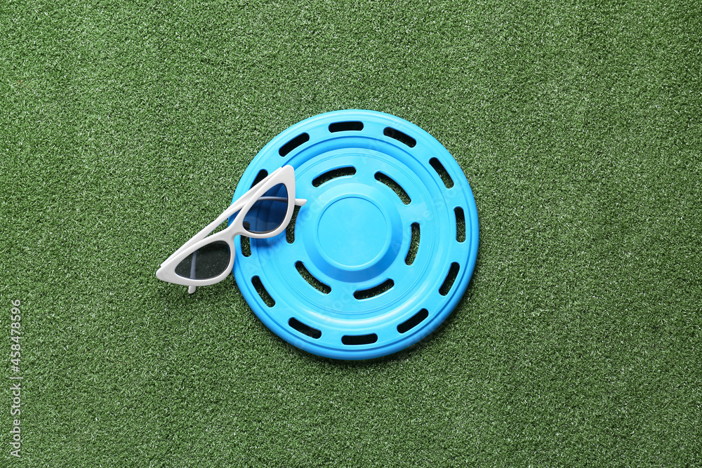 Frisbee disk and sunglasses on color background