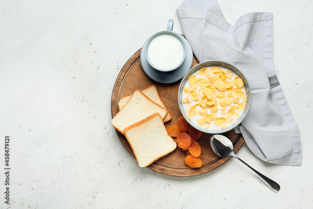 Bowl with tasty cornflakes, cup of milk, bread and dried apricots on light background