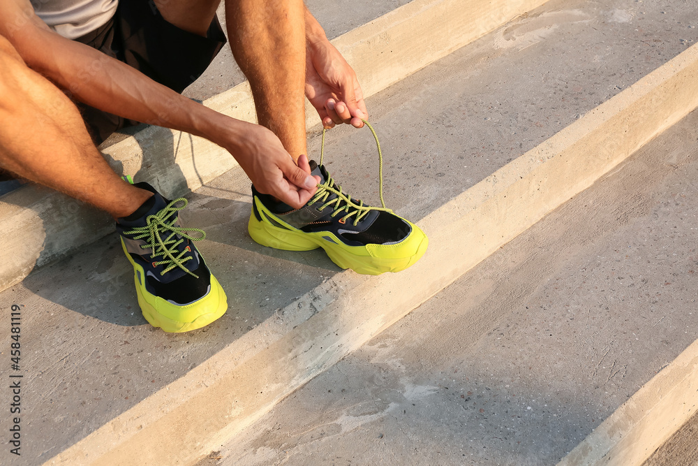 Sporty young man tying shoe laces outdoors