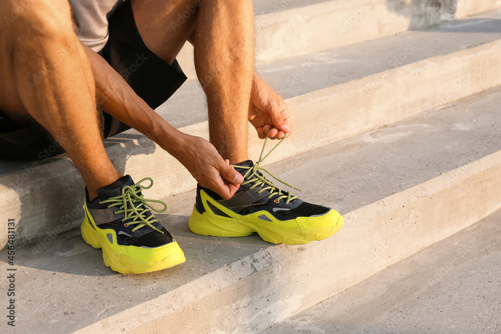 Sporty young man tying shoe laces outdoors