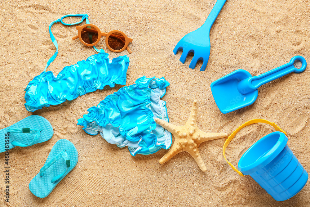 Set of beach accessories for children and stylish swimsuit on sand