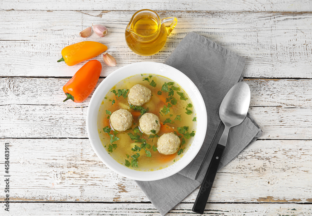 Bowl with tasty meatball soup, oil and spices on light wooden background