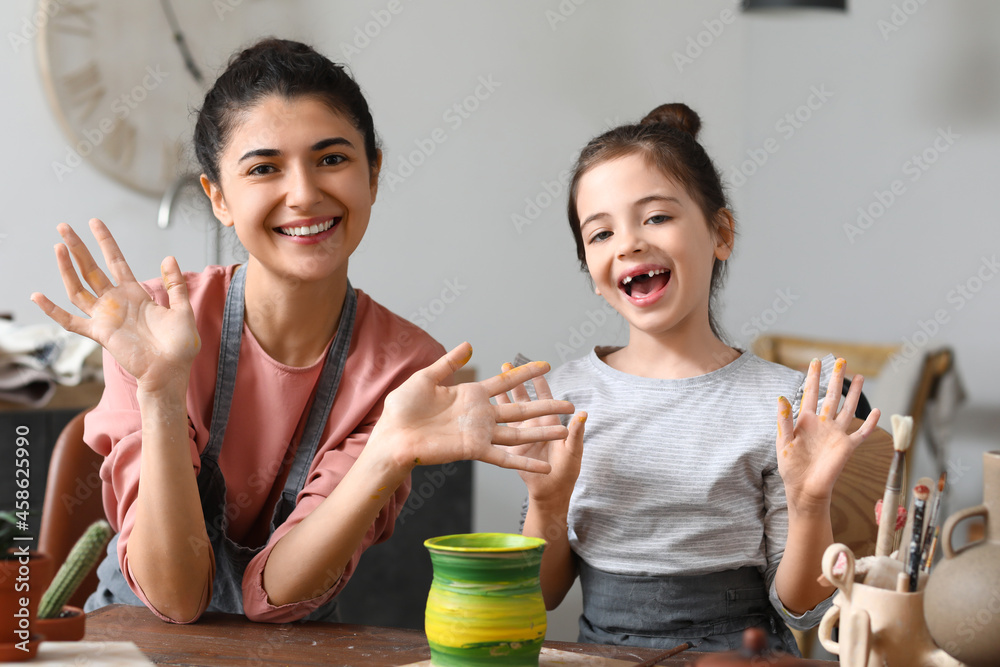 Little girl with her mother painting ceramic pot at home