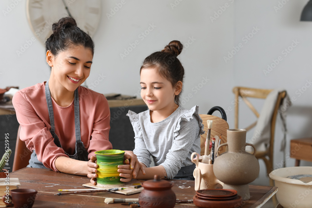 Little girl with her mother painting ceramic pot at home