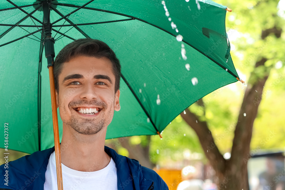 Handsome young man with umbrella in park on rainy day