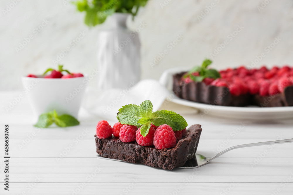 Spatula with piece of tasty raspberry pie and mint on light wooden table, closeup