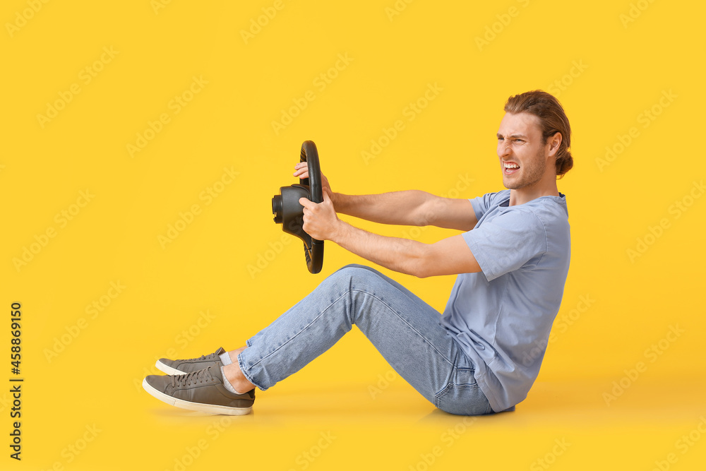 Angry young man with steering wheel on color background